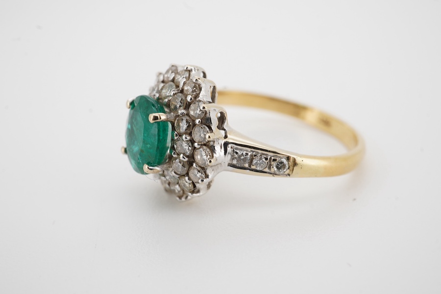 A modern 18ct, emerald and diamond set oval cluster ring with diamond set shoulders, size N/O, gross weight 4.1 grams. Condition - poor to fair